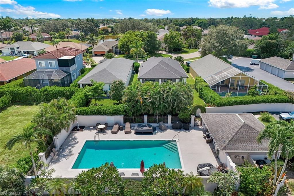 Aerial view of a neighborhood pool with a paved deck, lounge chairs, and surrounding homes.
