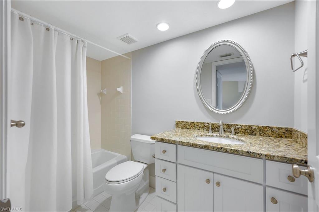 Bathroom with a curtained bathtub, white vanity, mottled granite countertop, and oval mirror.