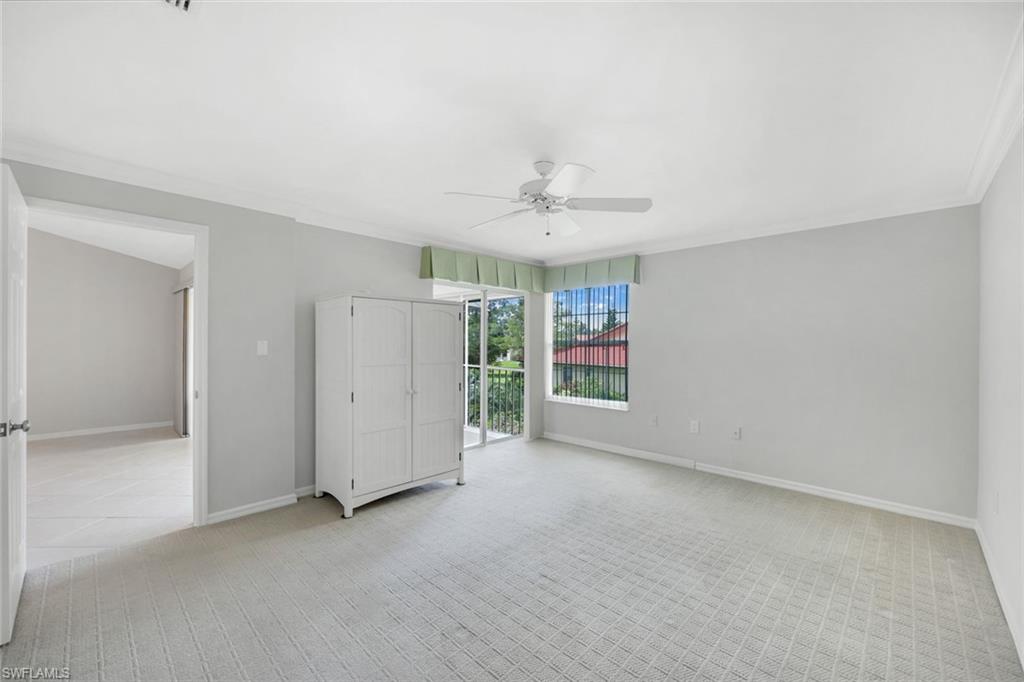Bright carpeted bedroom with a white armoire, ceiling fan, and balcony access.