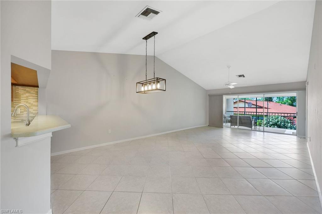 Empty living room with vaulted ceiling, tile floors, and sliding doors to a balcony.