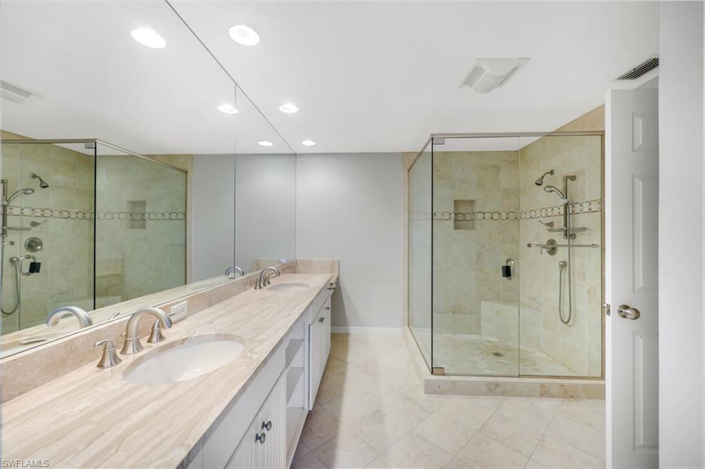 Primary bathroom with a marble double vanity and glass-enclosed stone-tile shower.