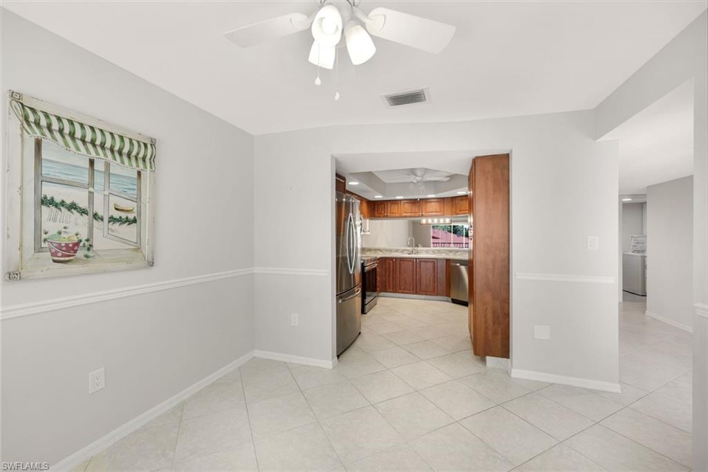 Empty tiled dining area opening into a wood-cabinet kitchen with stainless steel appliances.