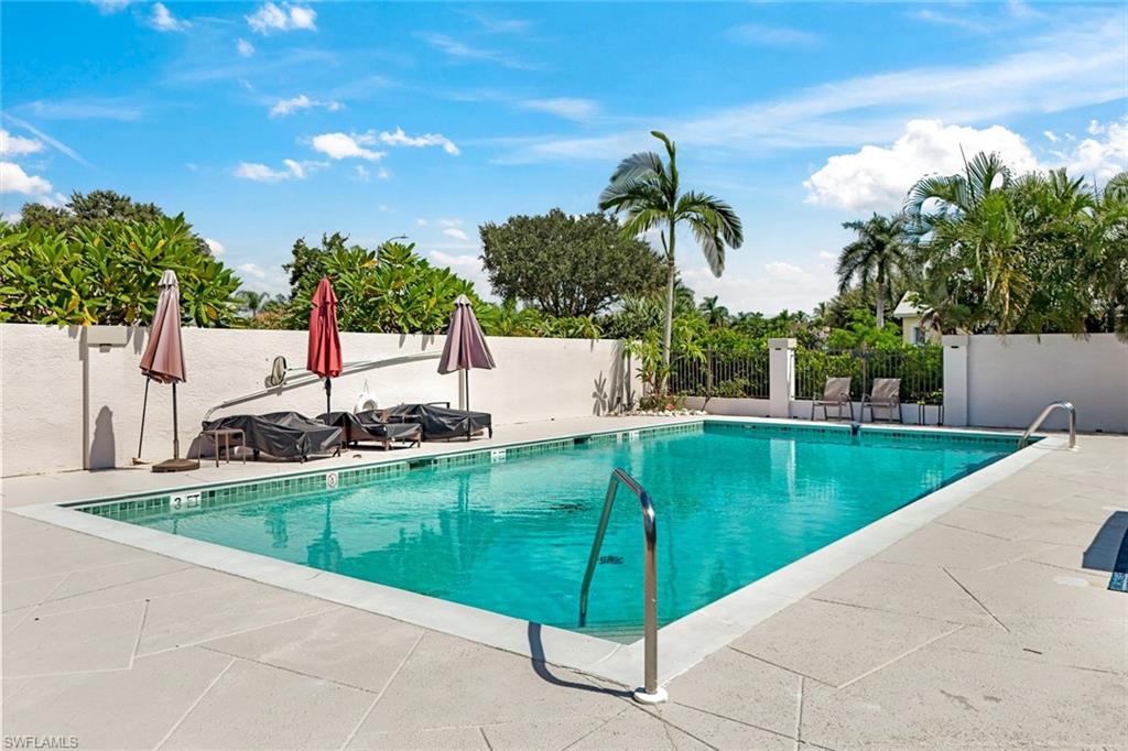Outdoor pool with turquoise water, lounge chairs, umbrellas, and palm trees.