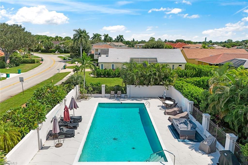 Aerial view of a community pool with lounge chairs, umbrellas, and palm trees.