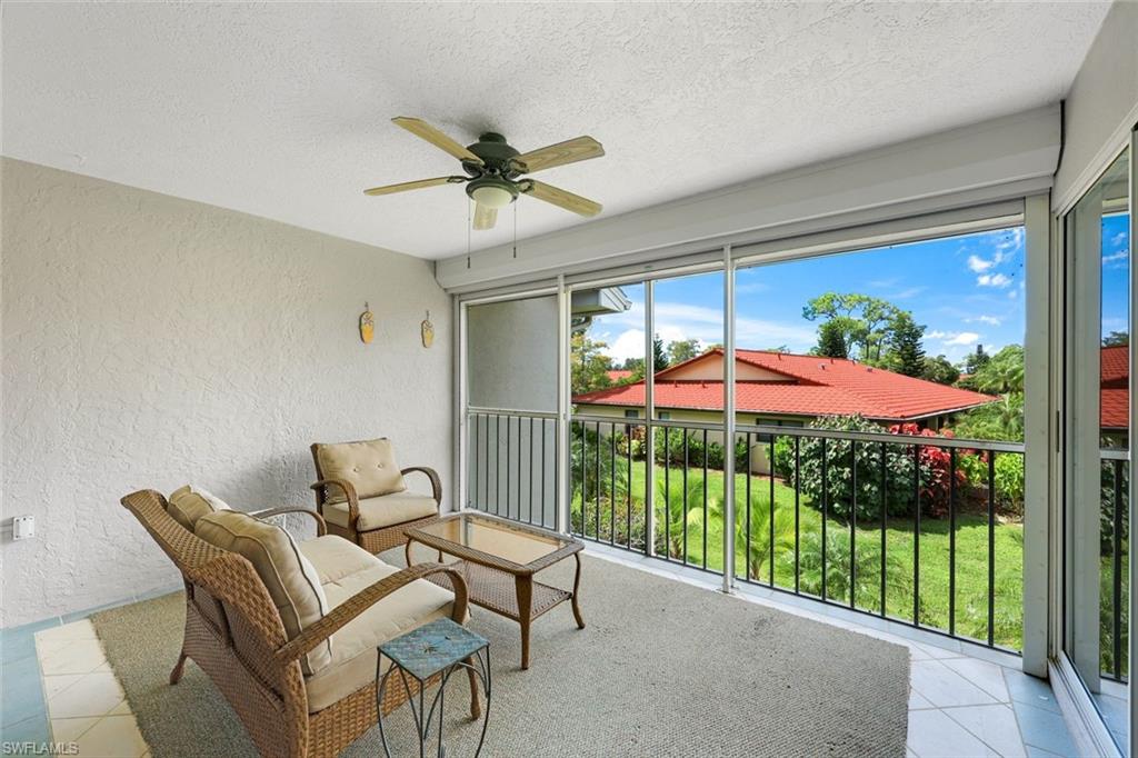 Covered balcony with wicker seating overlooking a landscaped lawn and neighboring red tile roof.