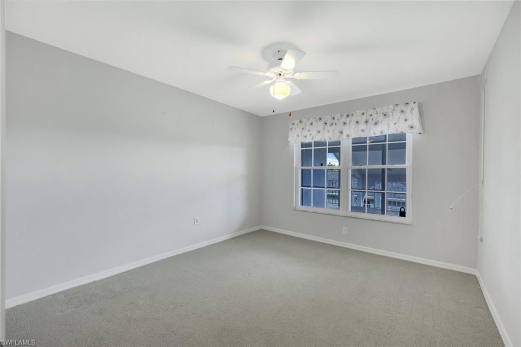 Empty carpeted room with a ceiling fan and windows overlooking water.