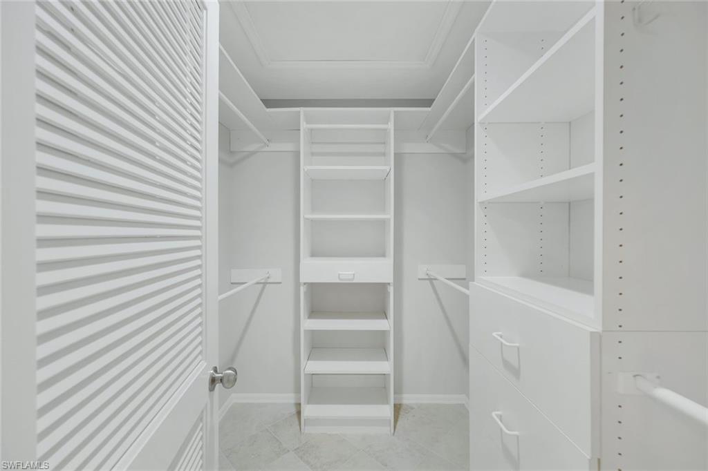 Walk-in closet with white built-in shelves, drawers, hanging rods, and a louvered door.