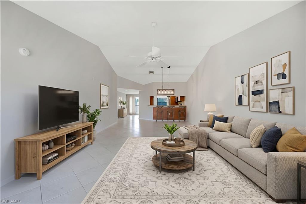 Staged living room with a long gray sofa, round wood coffee table, and open kitchen beyond.