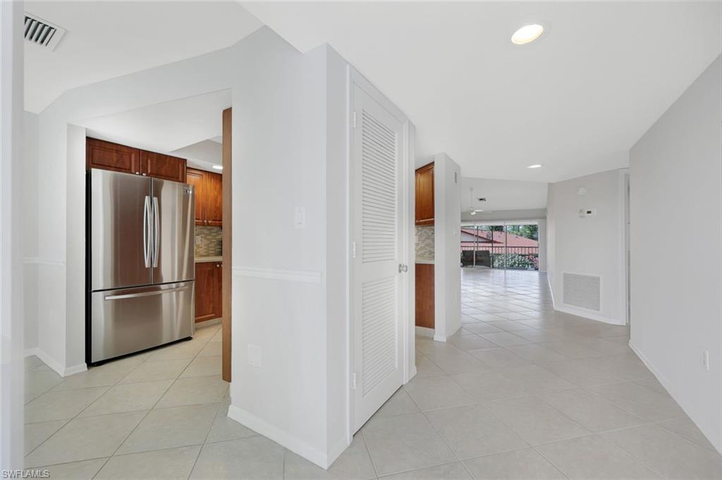Vacant condo kitchen with stainless steel refrigerator and wood cabinets opening to a tiled living area.