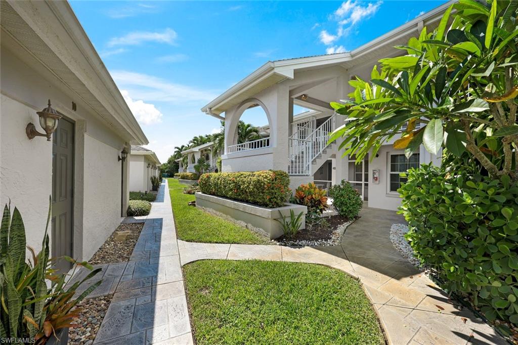 Condominium courtyard with a winding paved walkway, tropical landscaping, and stairs to a raised entrance.