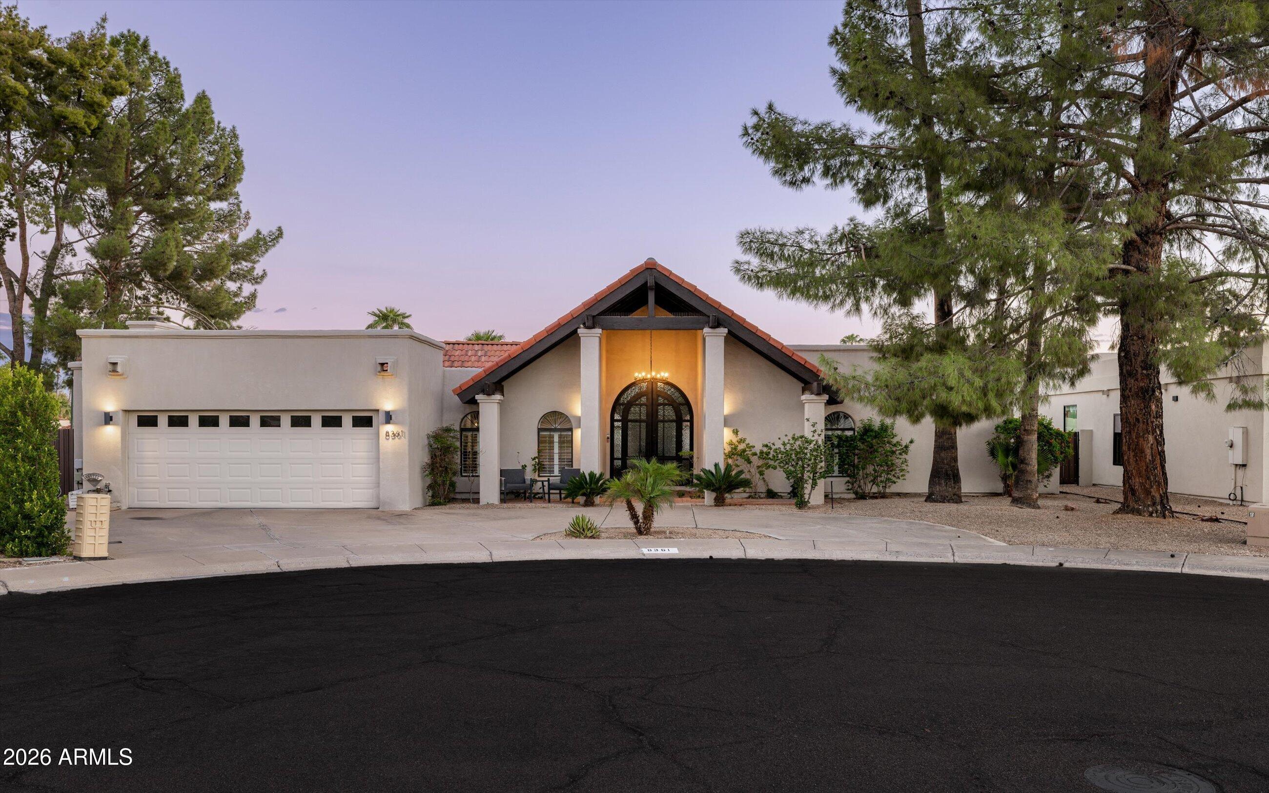 Stucco home with a red tile gabled entry, arched glass front door, and attached garage at dusk.