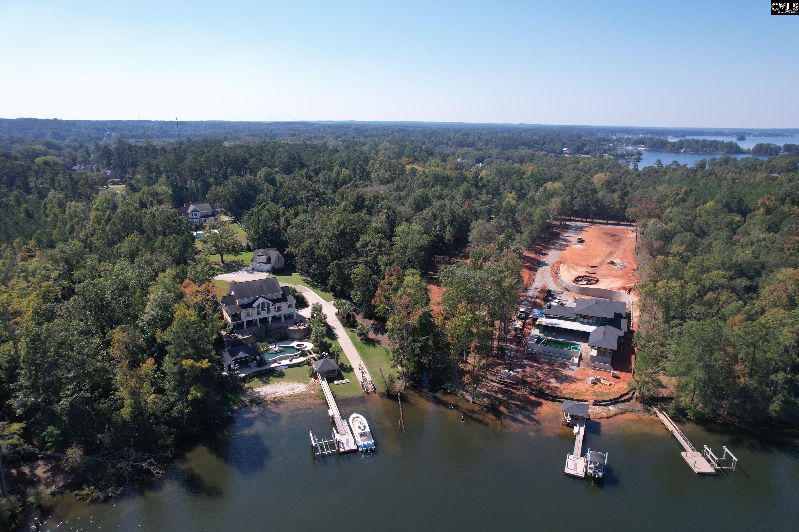 Aerial view of wooded lakefront homes with private docks, a pool, and an adjacent property under construction.