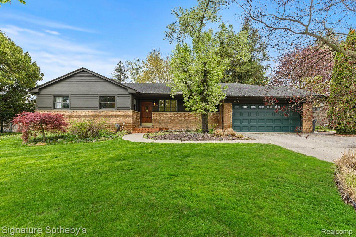 Single-story gray-and-brick home with a green double garage door and landscaped lawn.