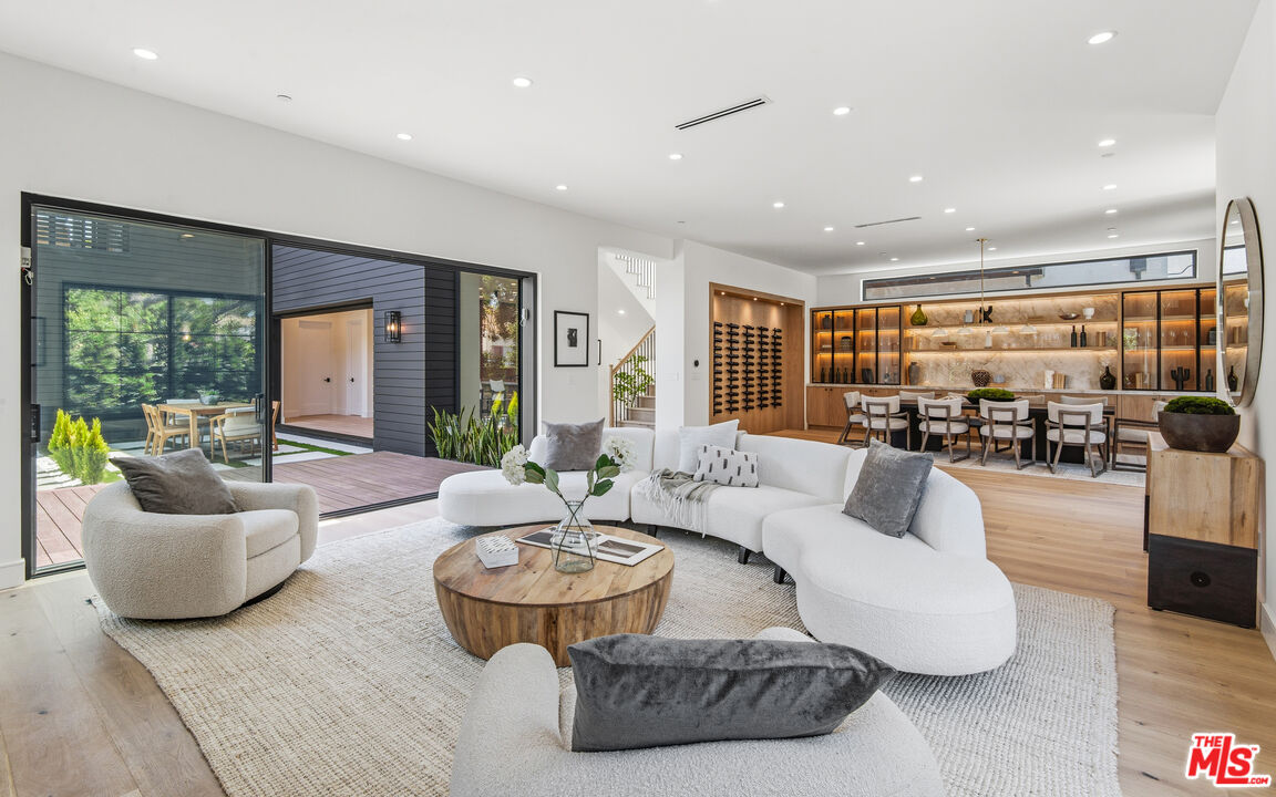 Open-plan living room with curved white seating, sliding doors to a deck, and an illuminated built-in bar.