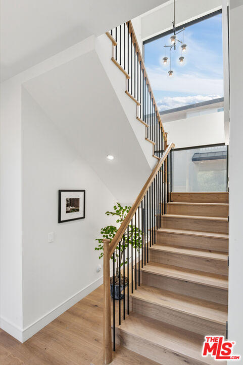 Modern light-wood staircase with black balusters beside a large window.