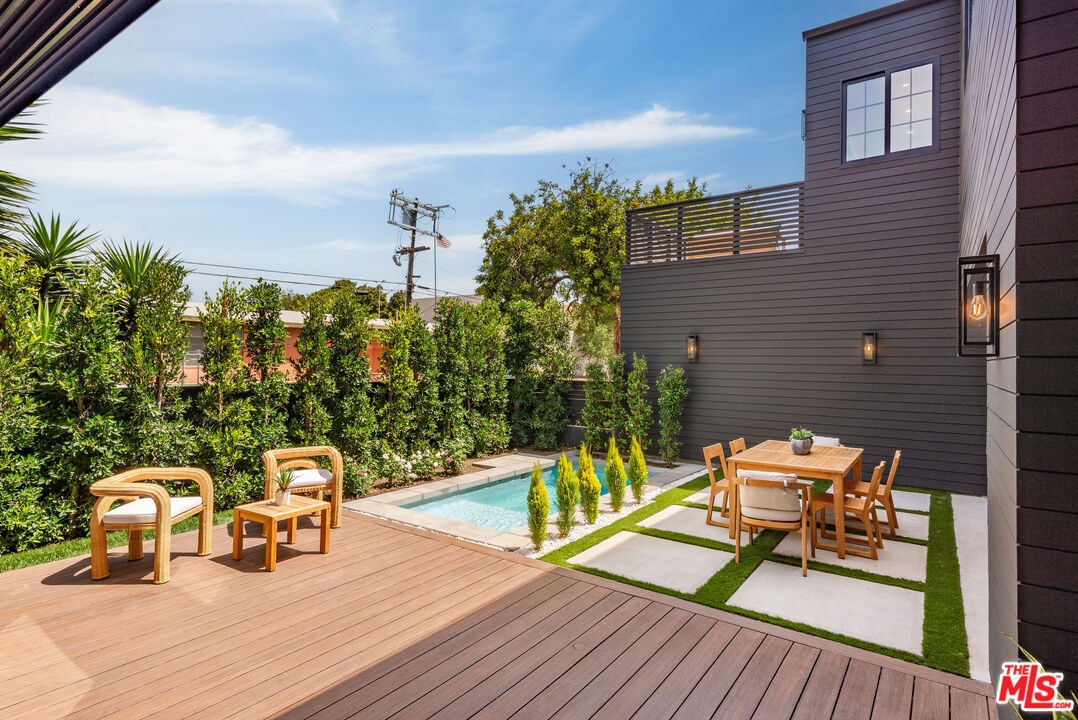 Modern backyard patio with a small pool, wood deck, and outdoor dining area.