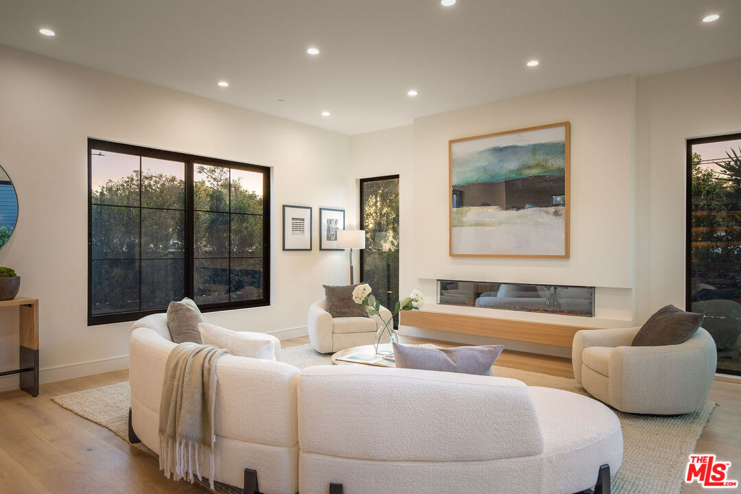 Staged living room with curved white seating, a linear fireplace, and large black-framed windows.