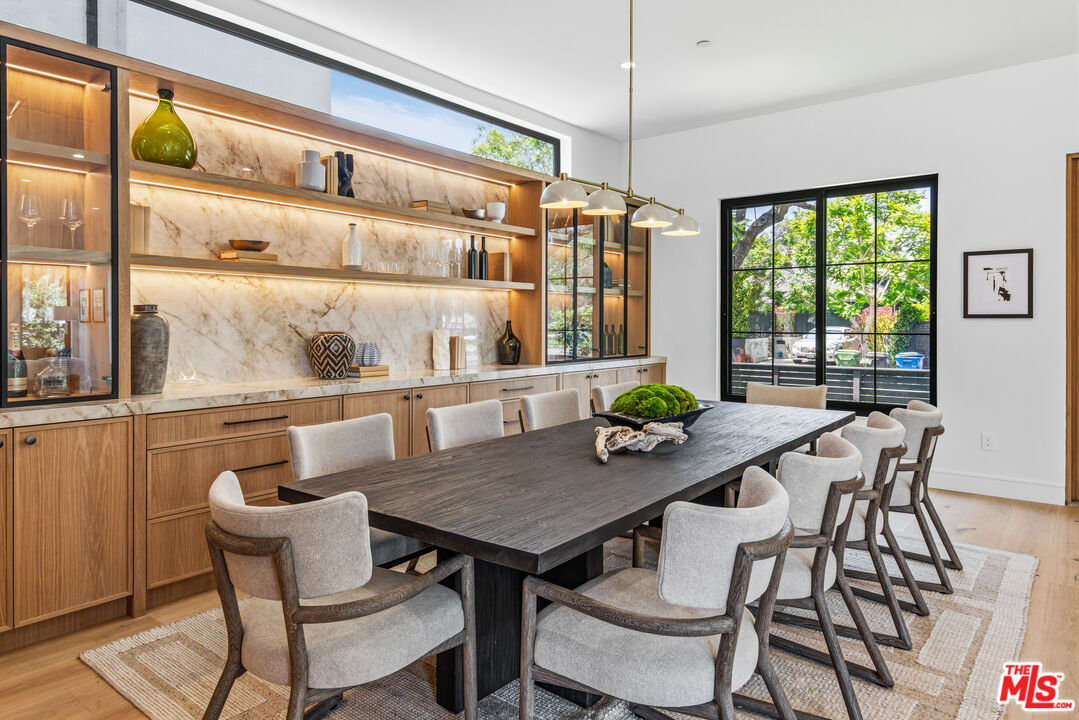 Dining room with a long dark wood table, upholstered chairs, and illuminated marble-backed shelving.