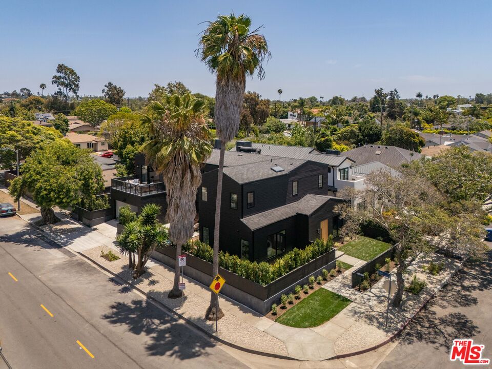 Modern black multi-story home on a landscaped corner lot, framed by tall palm trees.