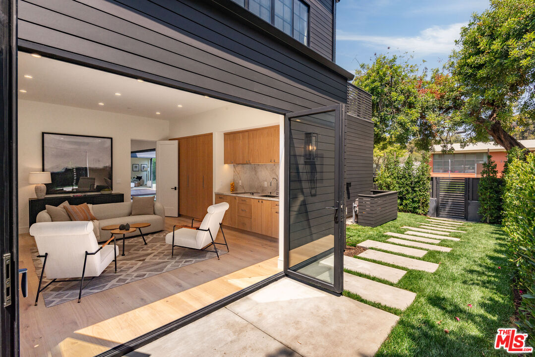Furnished modern living room opens through glass doors to a lawn and stepping-stone path.