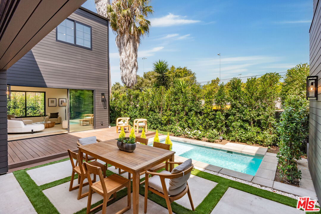 Modern home courtyard with a small pool, wooden dining set, and sliding doors to the living room.