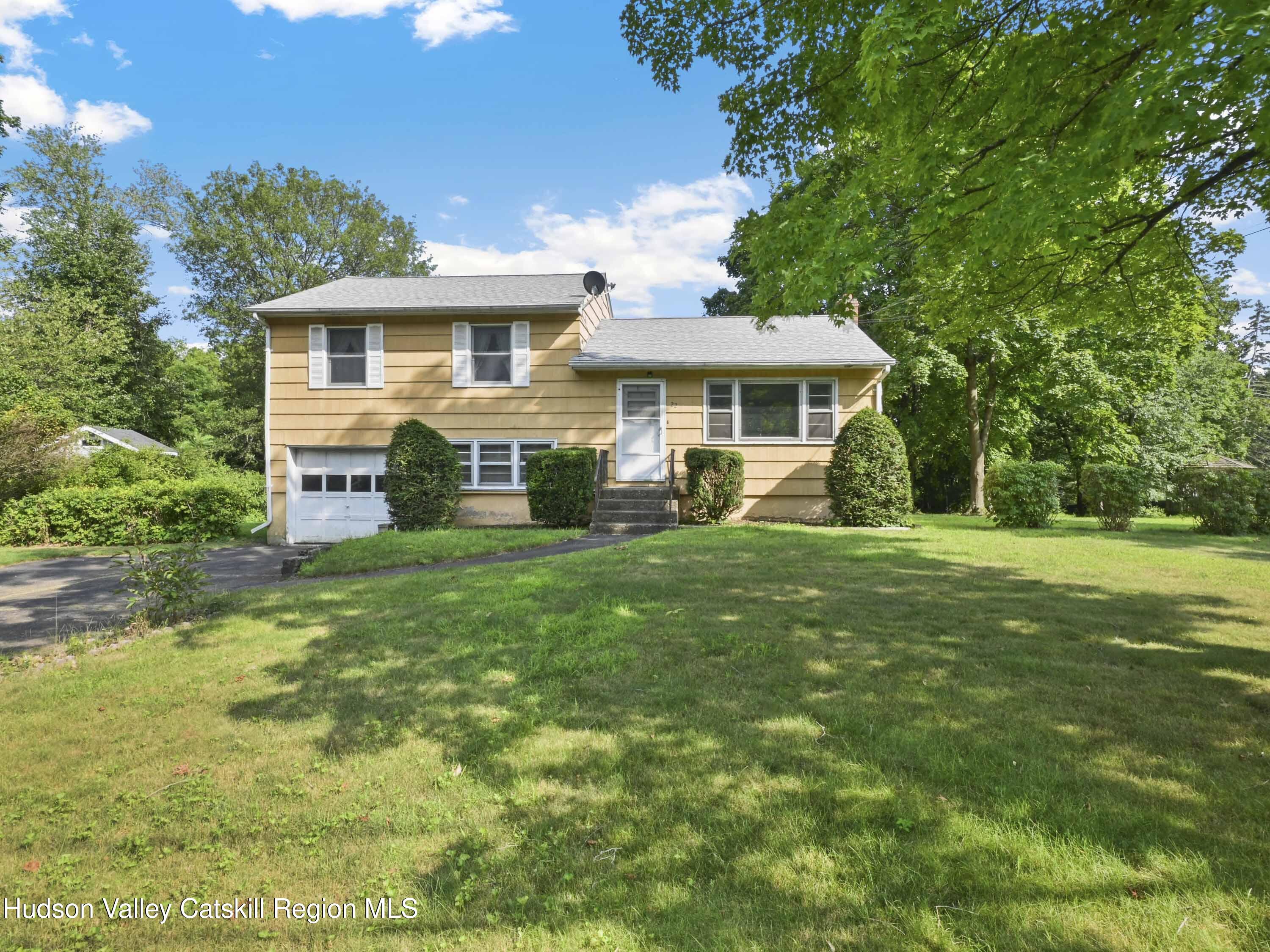 Tan split-level house with a single-car garage, front steps, and a shaded lawn.