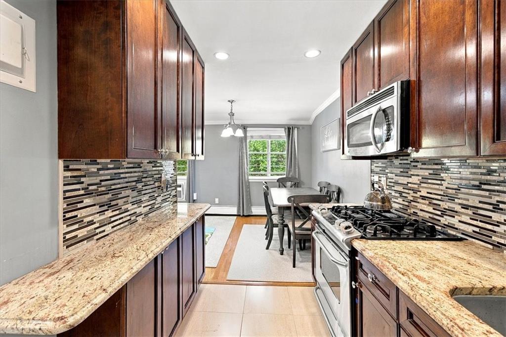 Galley kitchen with dark wood cabinets, granite counters, patterned backsplash, and a dining area.