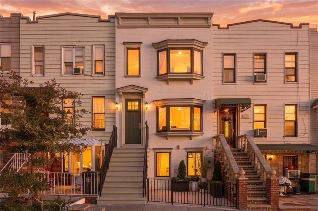 Attached townhouse with bay windows and a raised stoop, its windows glowing at golden hour.