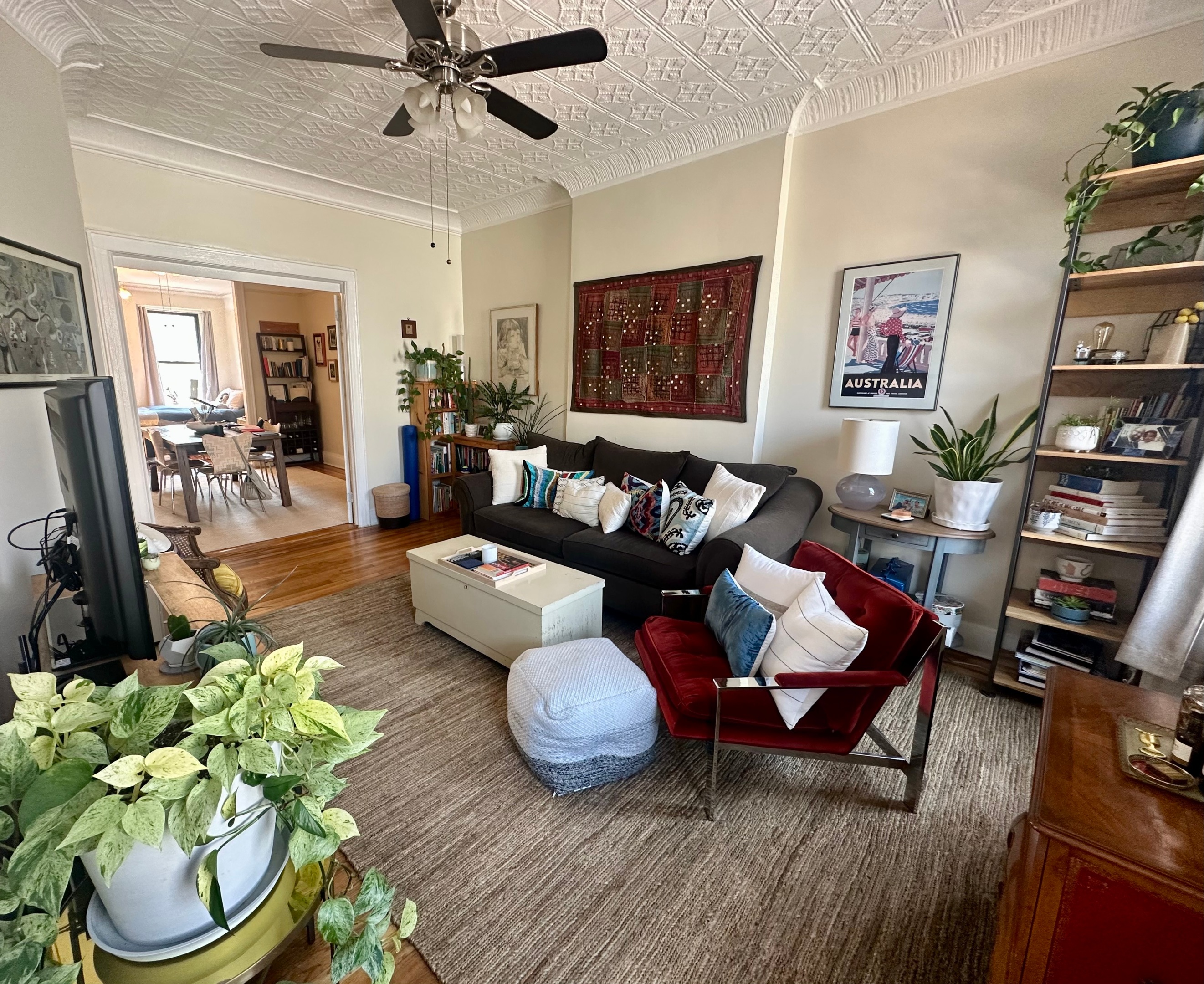 Living room with a patterned tin ceiling, dark sofa, red armchair, and hardwood floors.