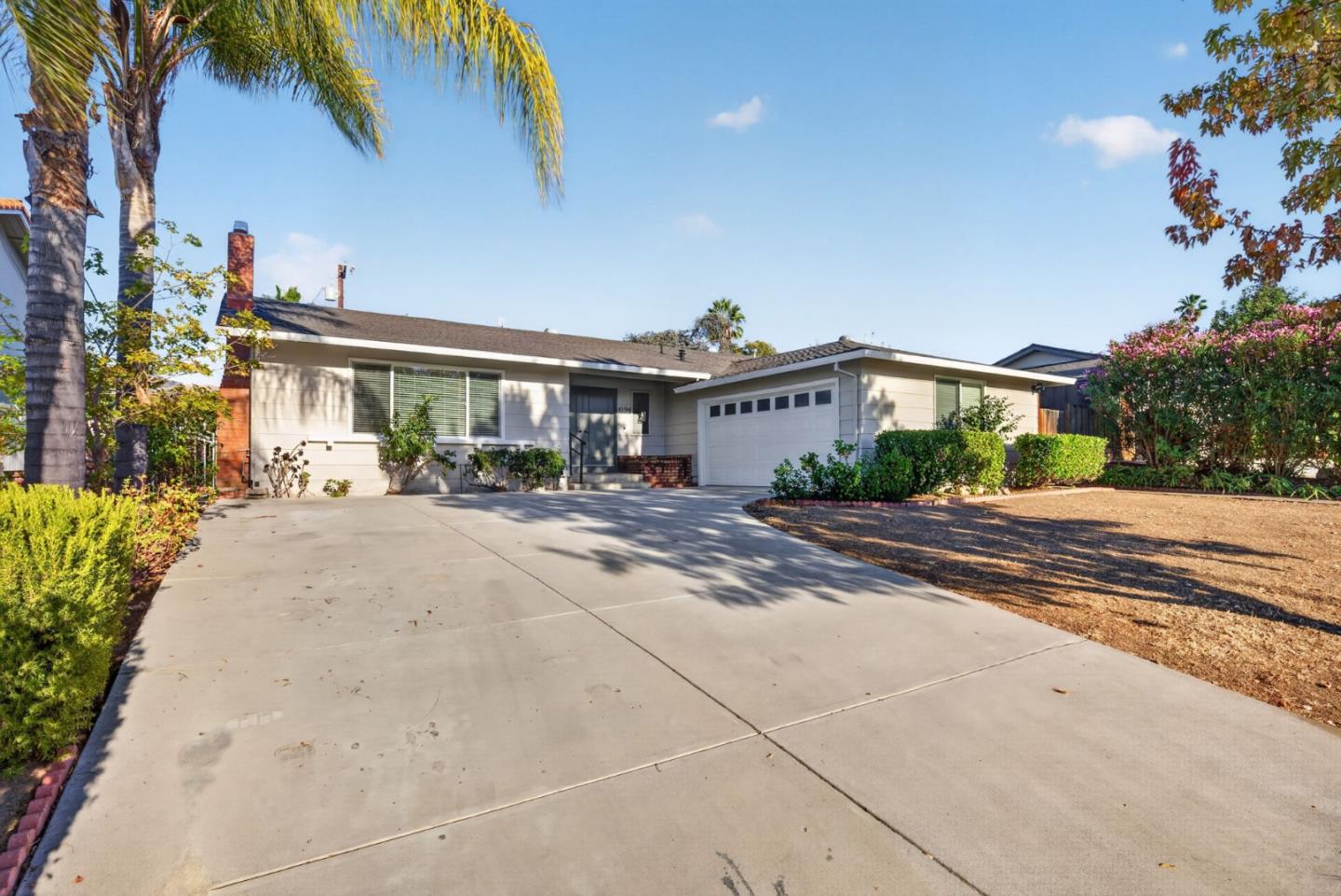 Single-story house with an attached garage, broad driveway, and palm trees.