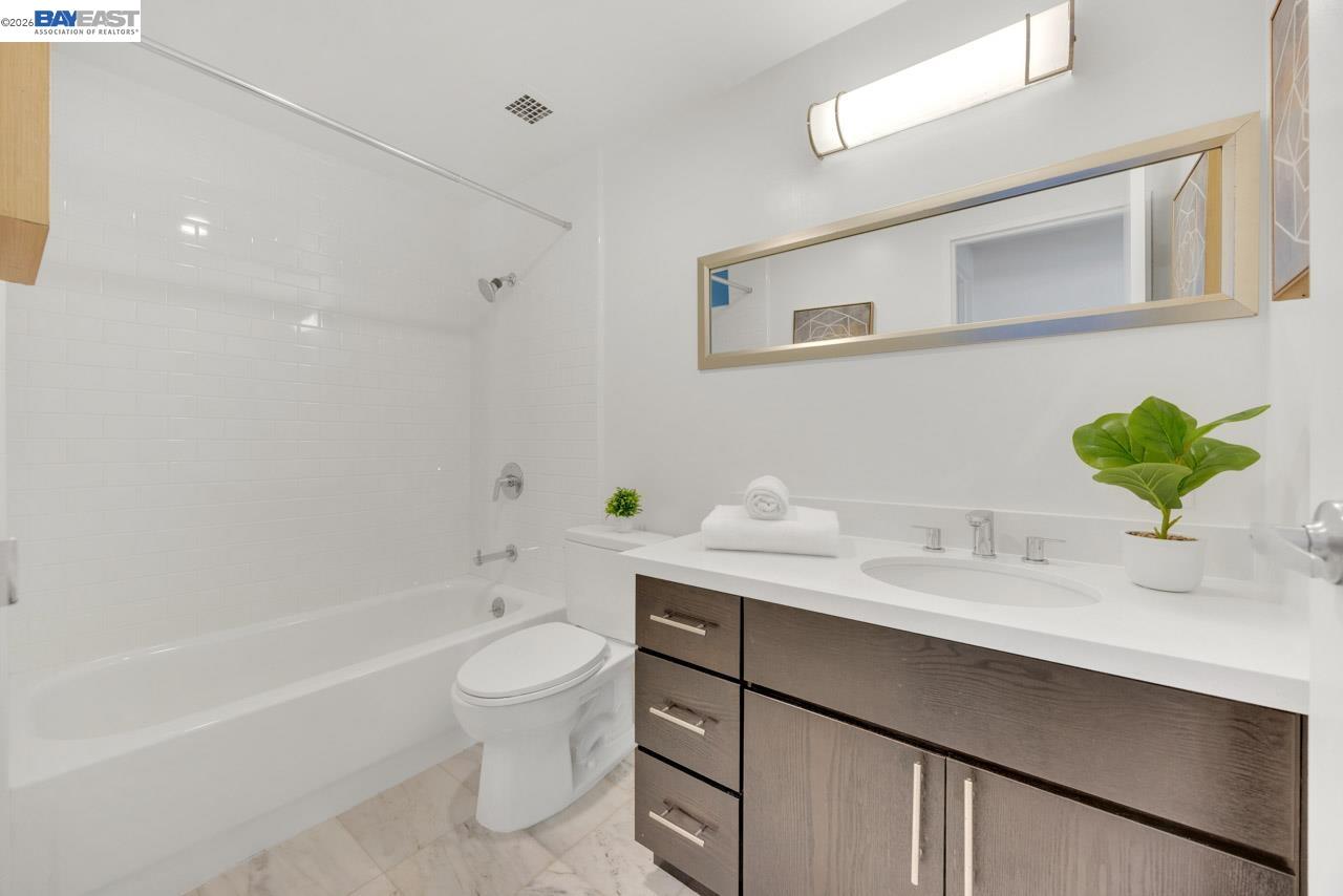 Staged bathroom with a white tub, dark wood vanity, wide mirror, and potted plants.
