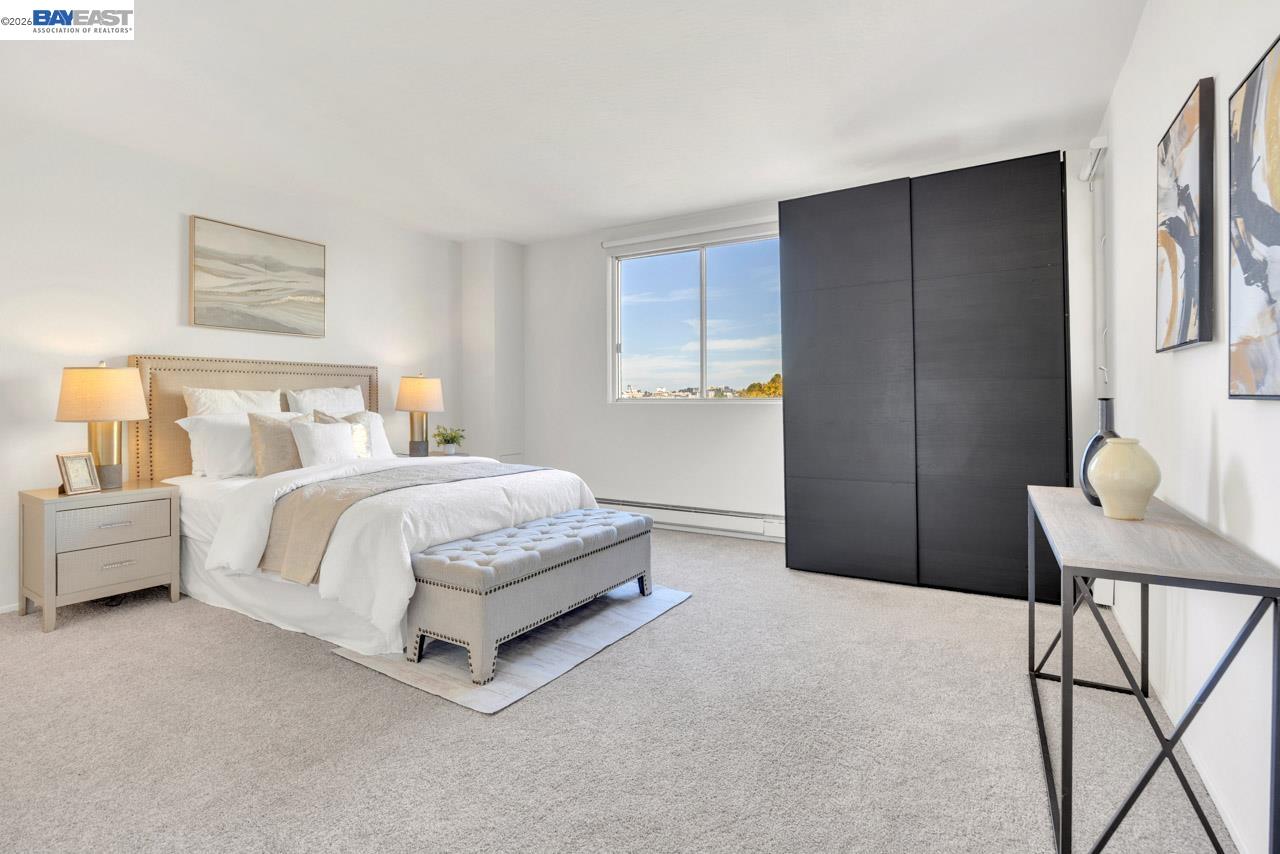 Furnished bedroom with a white bed, large dark wardrobe, and window overlooking distant buildings.