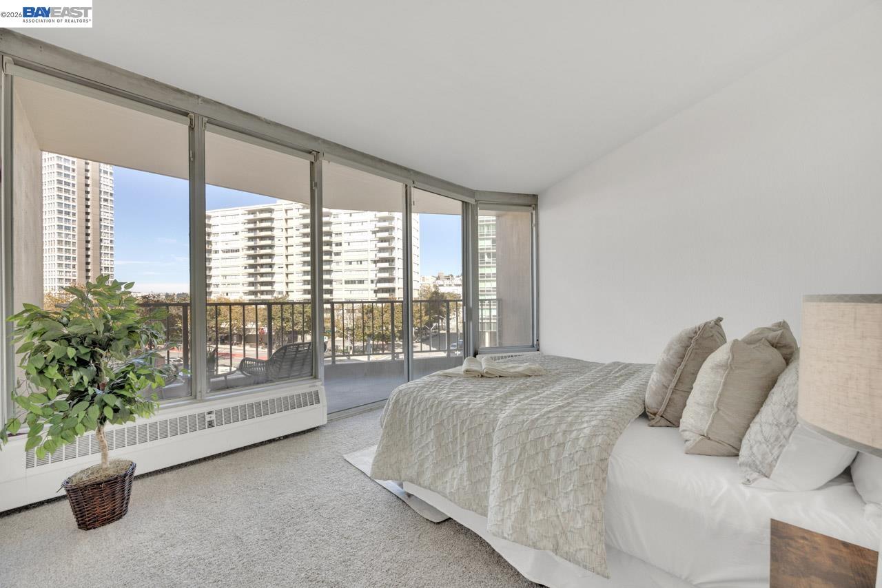Furnished bedroom with floor-to-ceiling windows overlooking nearby high-rise buildings.