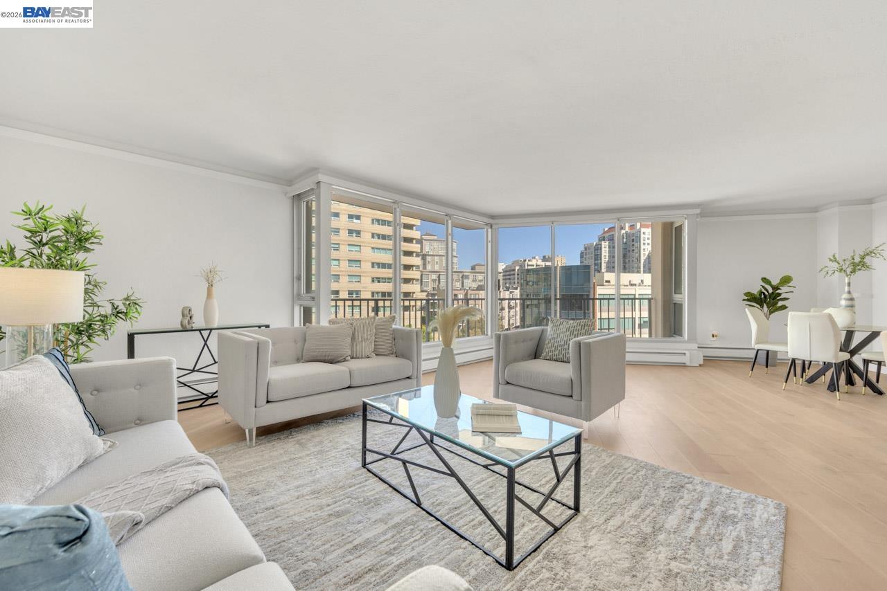 Staged living room with corner windows overlooking San Francisco buildings and a dining area.