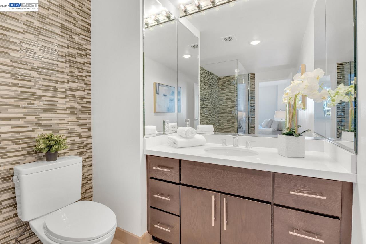 Modern bathroom with a wood vanity, mirrored wall, glass shower, and mosaic tile accent wall.
