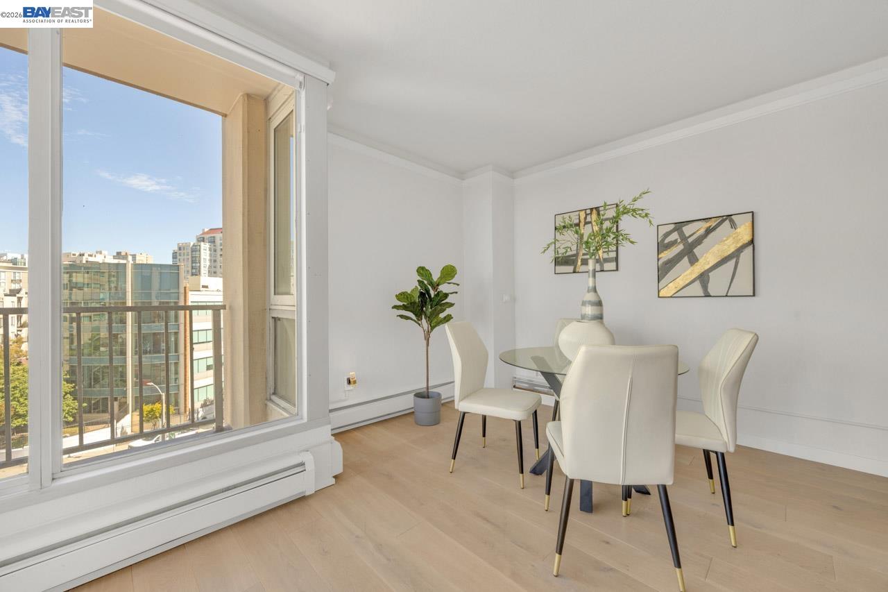 Dining area with a glass table and white chairs beside large windows overlooking nearby city buildings.