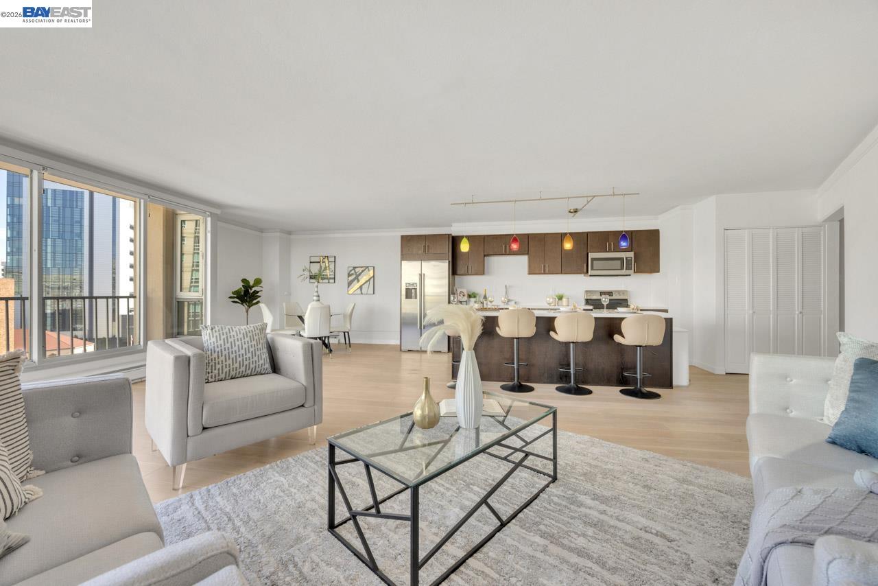Staged open-plan living room and kitchen with colorful pendant lights and city views through large windows.