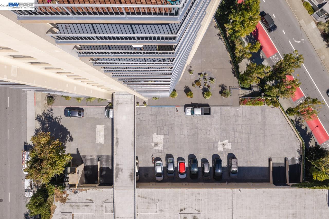 Aerial view of a multistory building and its parking area beside a tree-lined street.