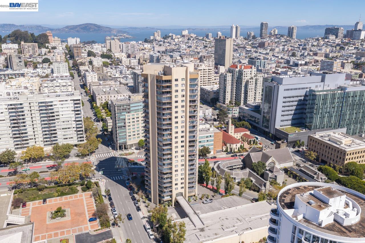 San Francisco high-rise tower amid downtown buildings, with the bay visible in the distance.