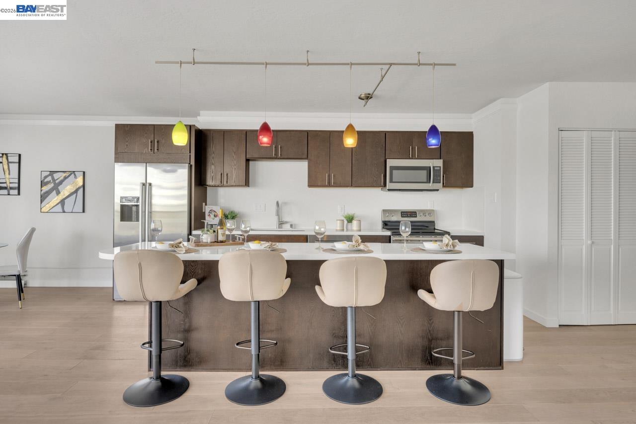 Kitchen with dark wood cabinets, stainless steel appliances, and an island with four cream bar stools.