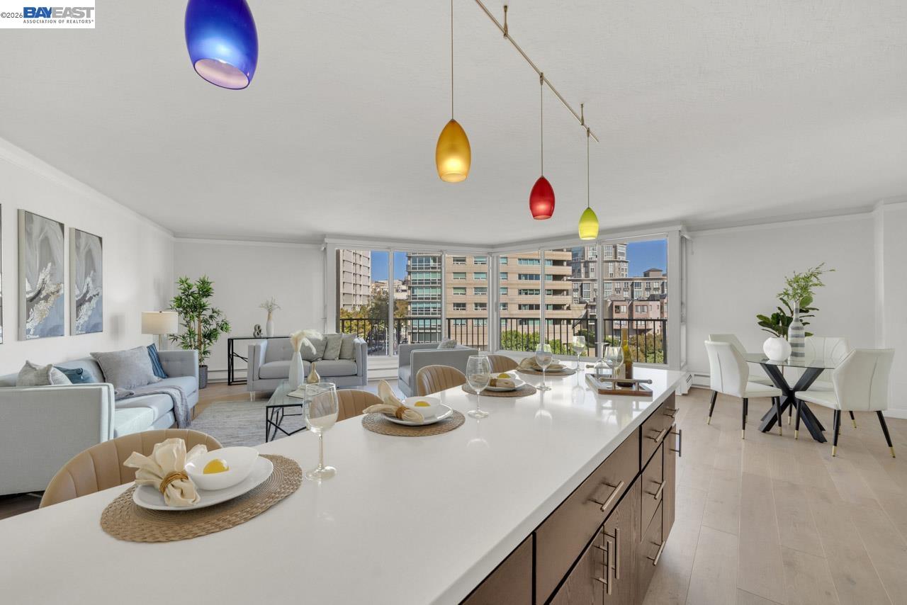 Open-plan kitchen and living room with a long island, colorful pendant lights, and city buildings beyond the windows.