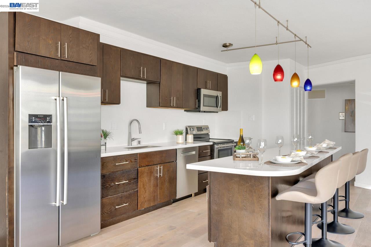 Modern kitchen with dark wood cabinetry, stainless steel appliances, and colorful pendant lights over a white island.