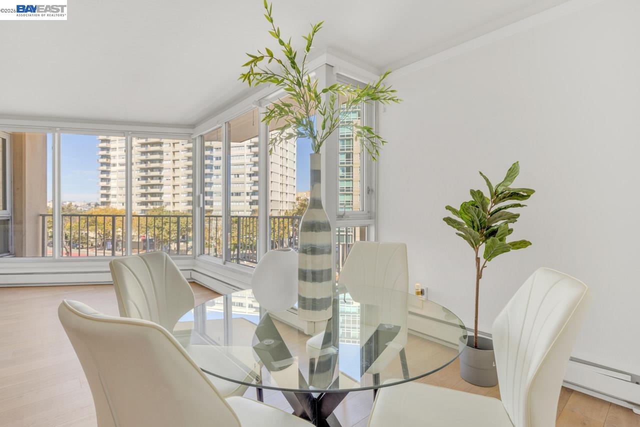 Dining area with a glass table and corner windows overlooking city buildings.