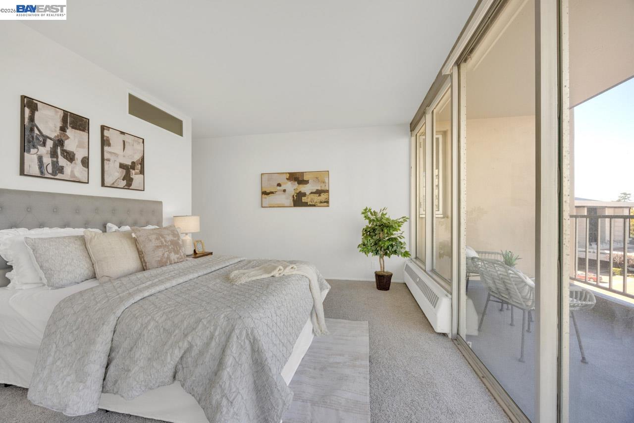 Staged bedroom with a gray upholstered bed and sliding glass doors to a balcony.