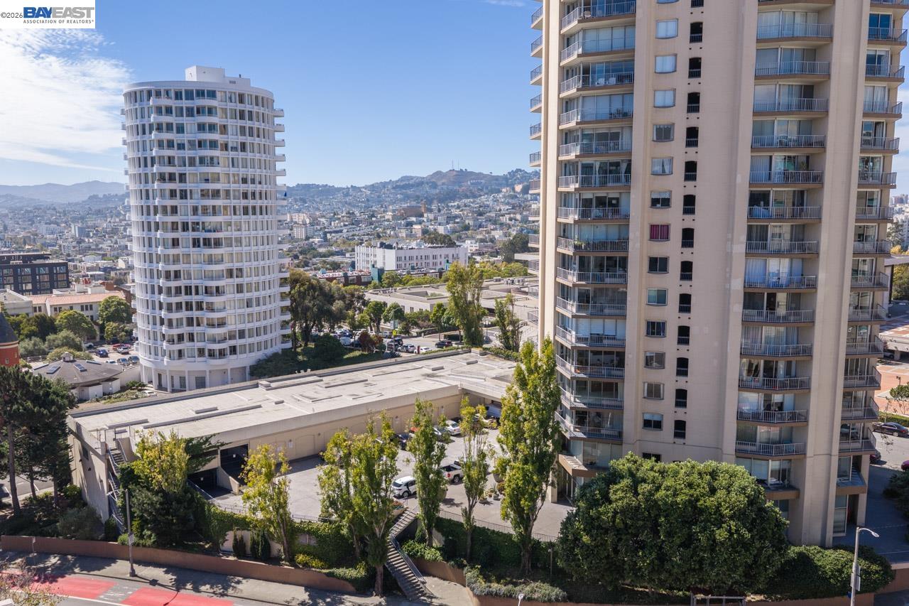 High-rise residential building beside a rounded tower, with San Francisco hills and city blocks beyond.