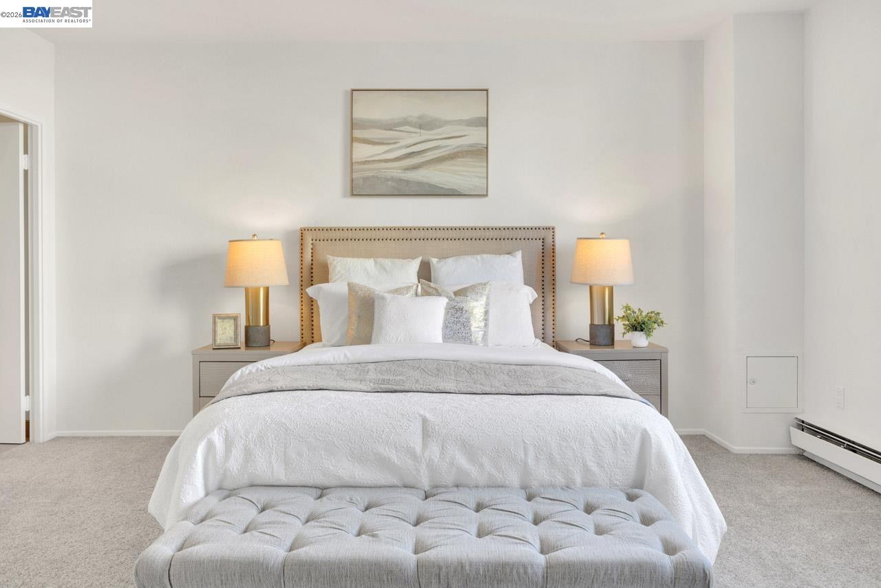 Staged bedroom with white bedding, a tufted bench, matching bedside lamps, and framed abstract art.