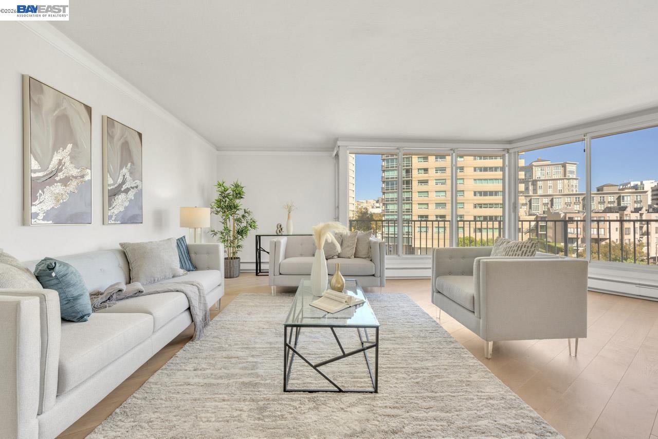 Staged living room with white seating, a glass coffee table, and large windows overlooking city buildings.