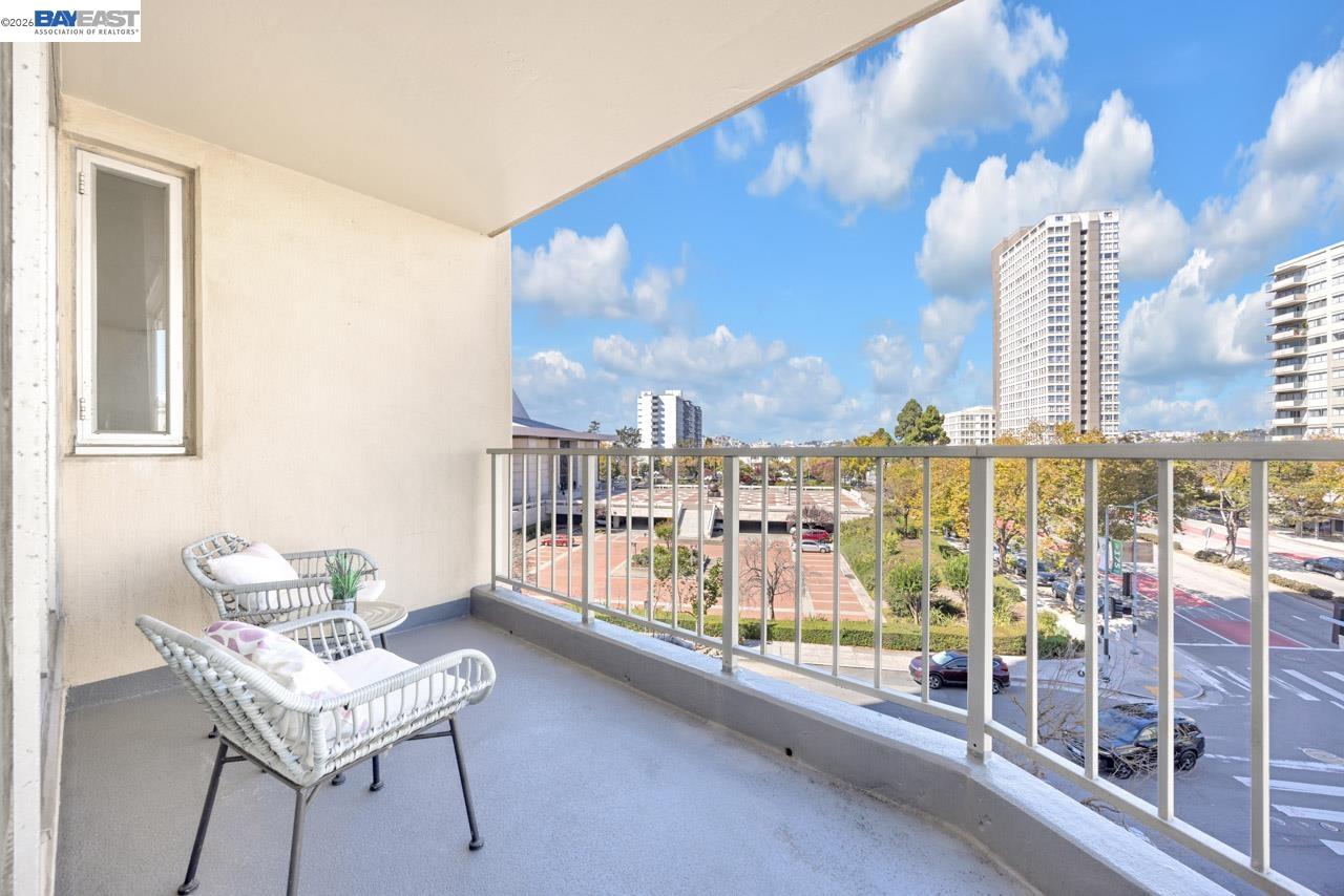 Apartment balcony with wicker seating overlooking San Francisco streets and high-rise buildings.