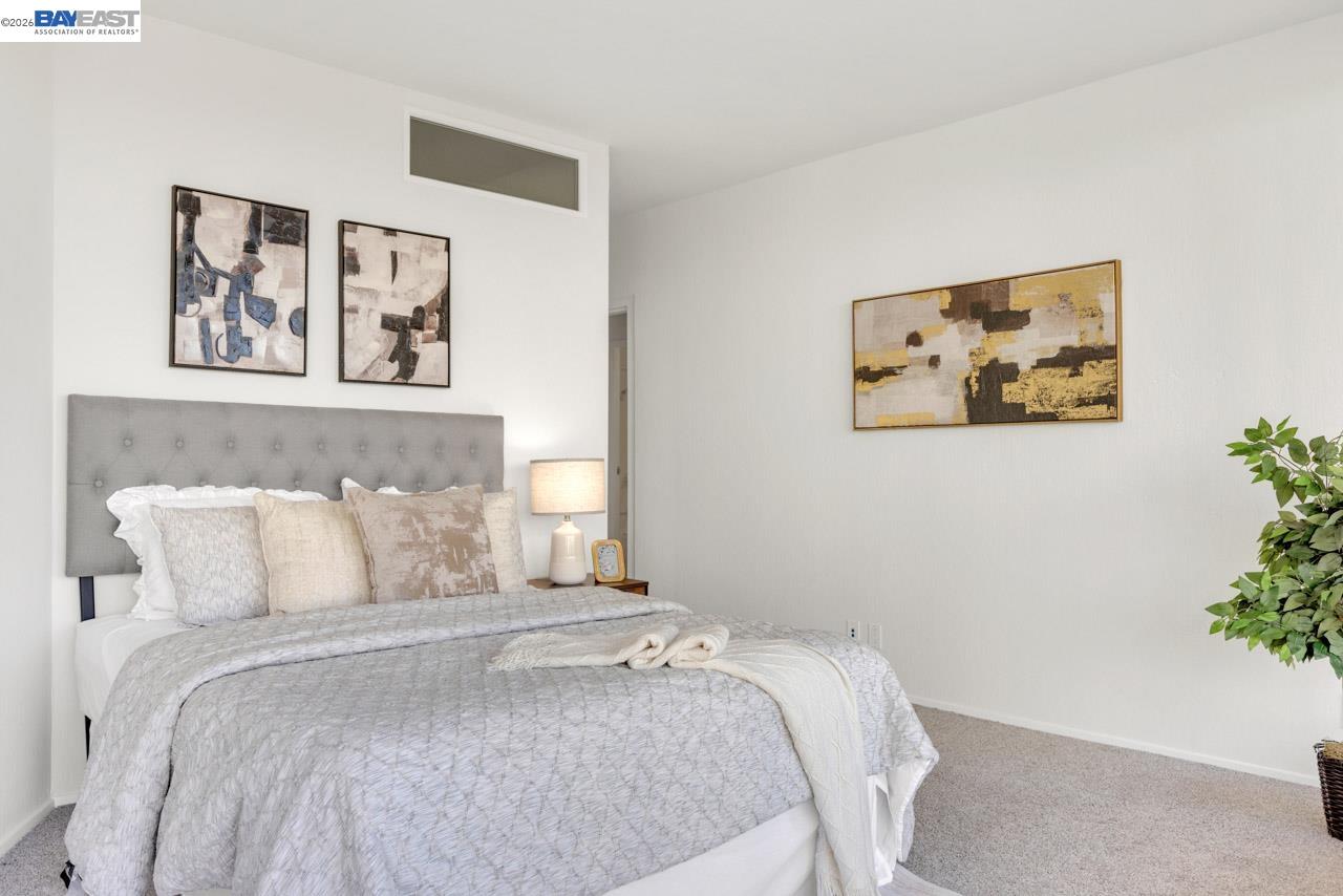 Staged bedroom with a tufted gray headboard, pale bedding, abstract art, and a bedside lamp.