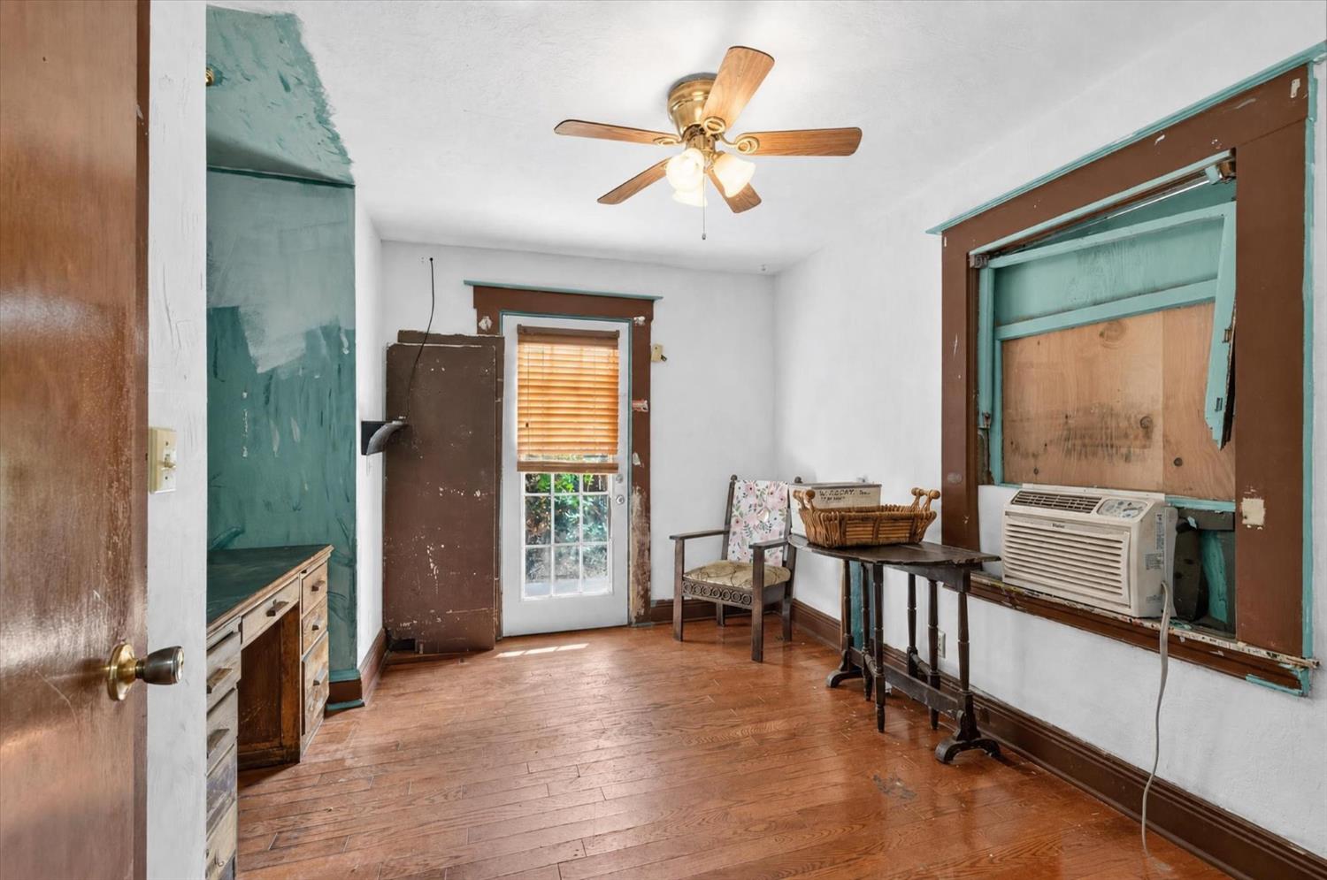 Room with worn wood floors, distressed turquoise trim, and a window air conditioner.